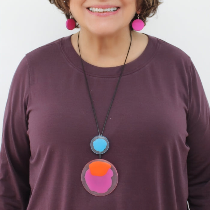 Person wearing a purple shirt with a colorful necklace against a white background