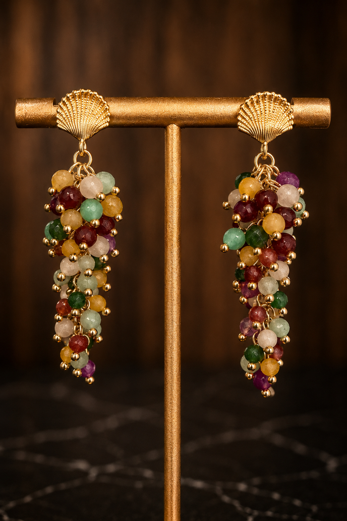 Close-up of Raelynn gemstone cascade earrings with multicolored natural gemstones and 18kt gold-plated shell posts.