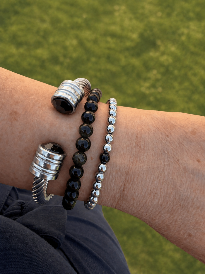 Wrist wearing three bracelets with a blurred green background