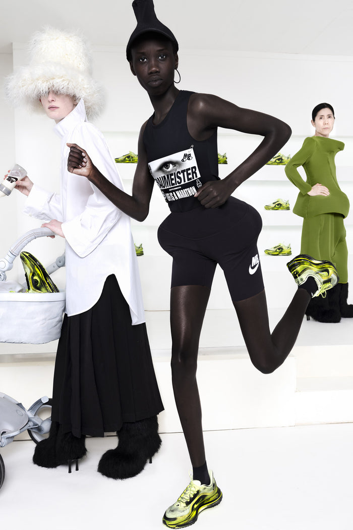 Model wearing black outfit with Nike shoes in a studio setting