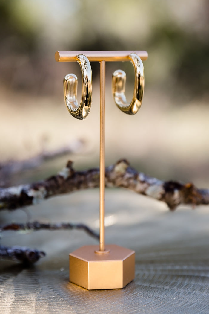 Gold high polish sculptural hoop earrings displayed on stand