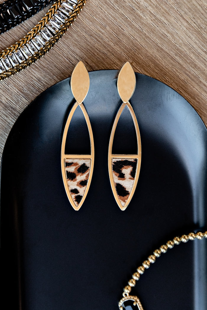 Gold earrings with leopard print details on a black surface