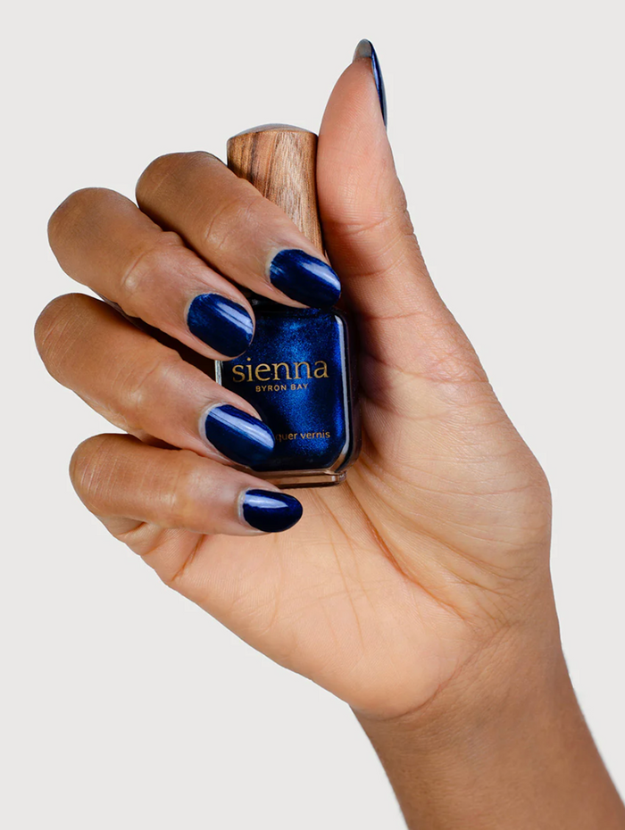 Hand holding a blue nail polish bottle with 'sienna' branding.