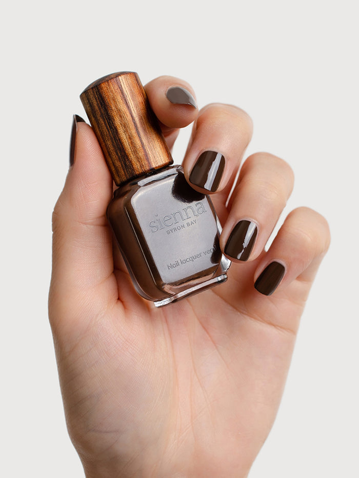 Hand holding a bottle of nail polish with wooden cap on a light background