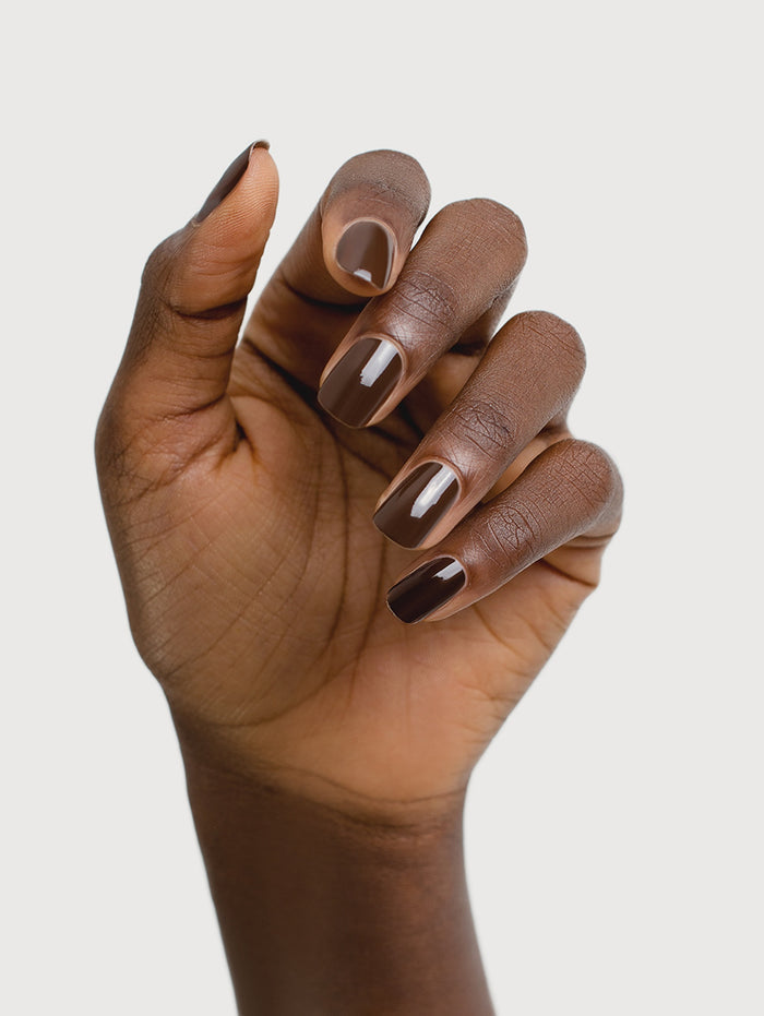 Hand with dark brown nail polish on a light gray background