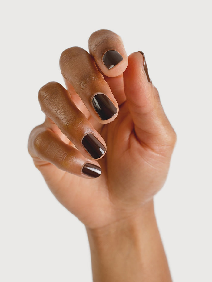 Hand with dark nail polish on a light background
