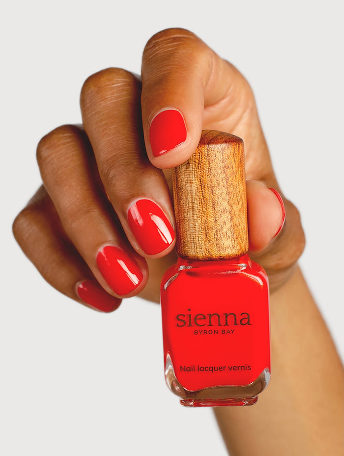 Hand holding a bottle of red nail polish with 'sienna' branding.