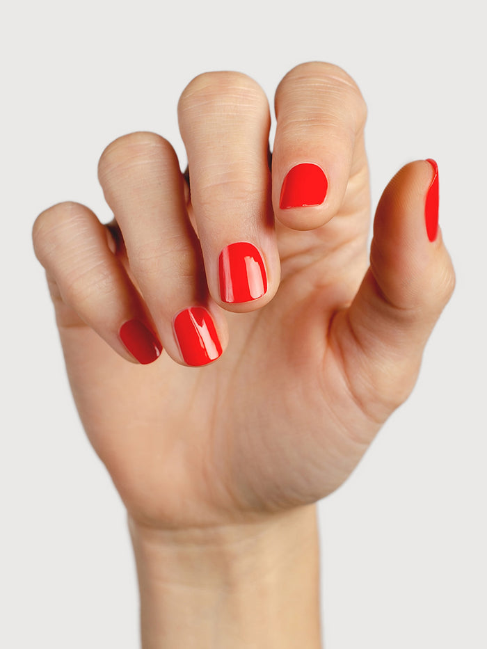 Hand with red nail polish on a light gray background