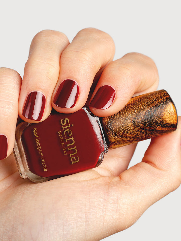 Hand holding a bottle of Sienna nail polish with red nail polish on nails.