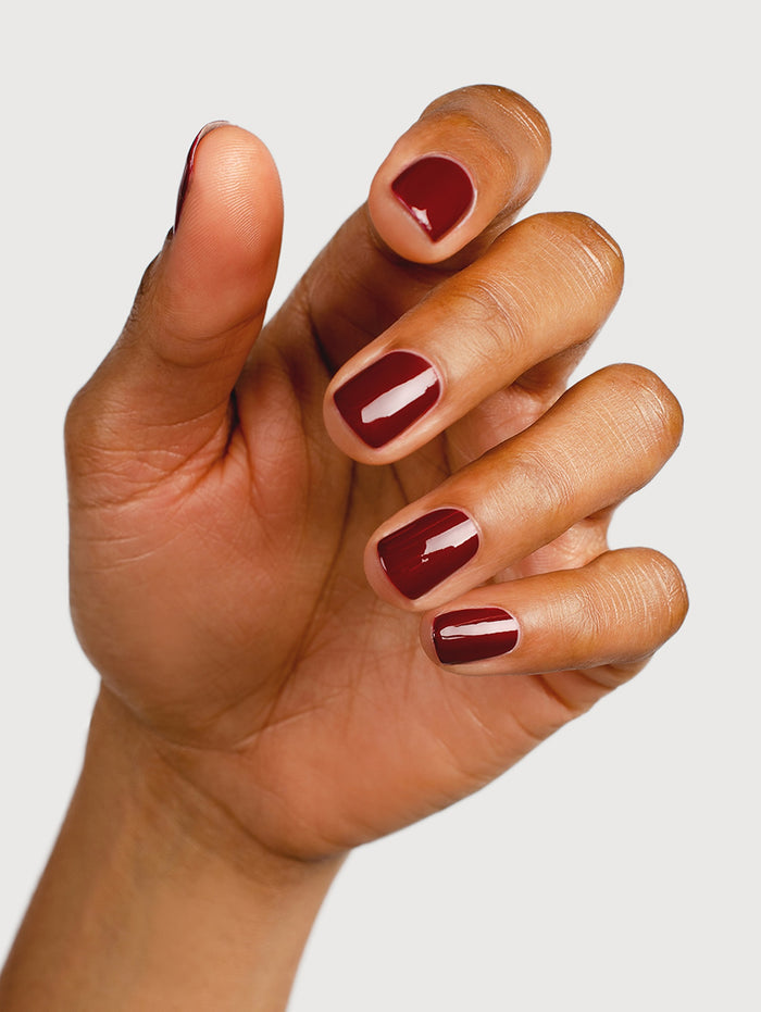 Hand with maroon nail polish on a plain background
