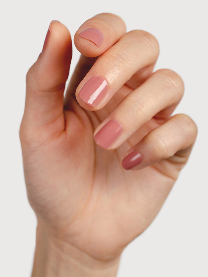 Hand with pink nail polish on a plain background