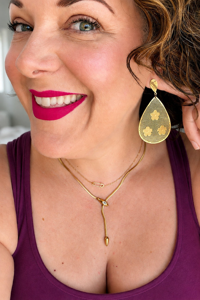 Selfie of Erin Markland wearing a tank top and Soleri Statement Earrings with the Delicate Salama Necklace layered with other gold necklaces, highlighting the dainty safety pin pendant and effortless everyday style.