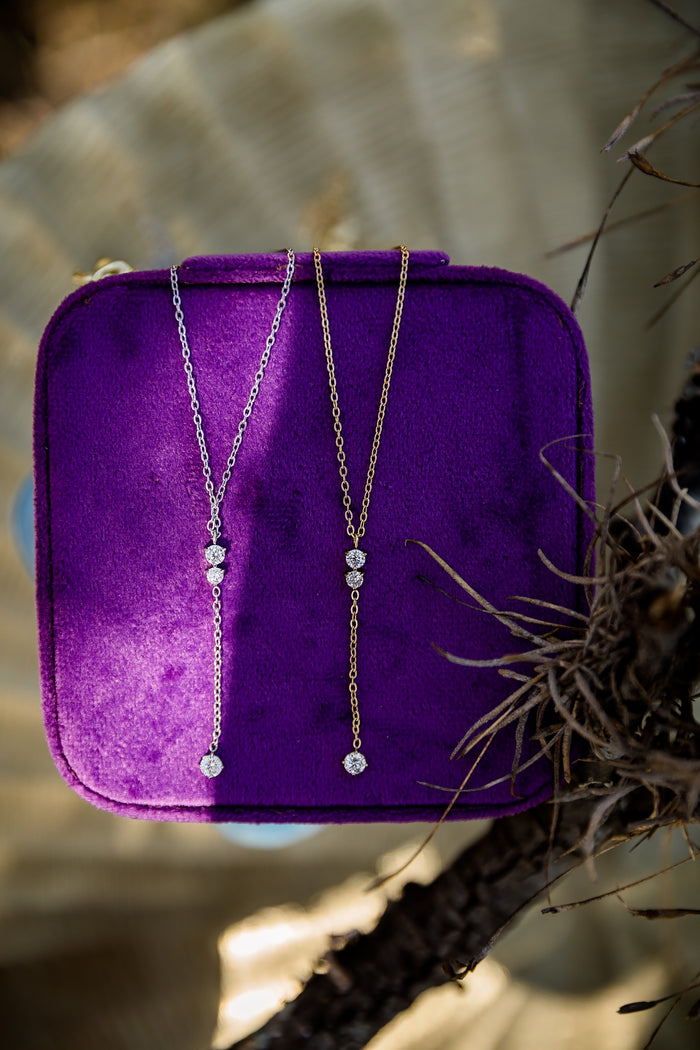 Two dainty necklaces on a purple velvet stand with a natural background