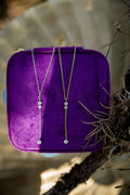 Two dainty necklaces on a purple velvet stand with a natural background