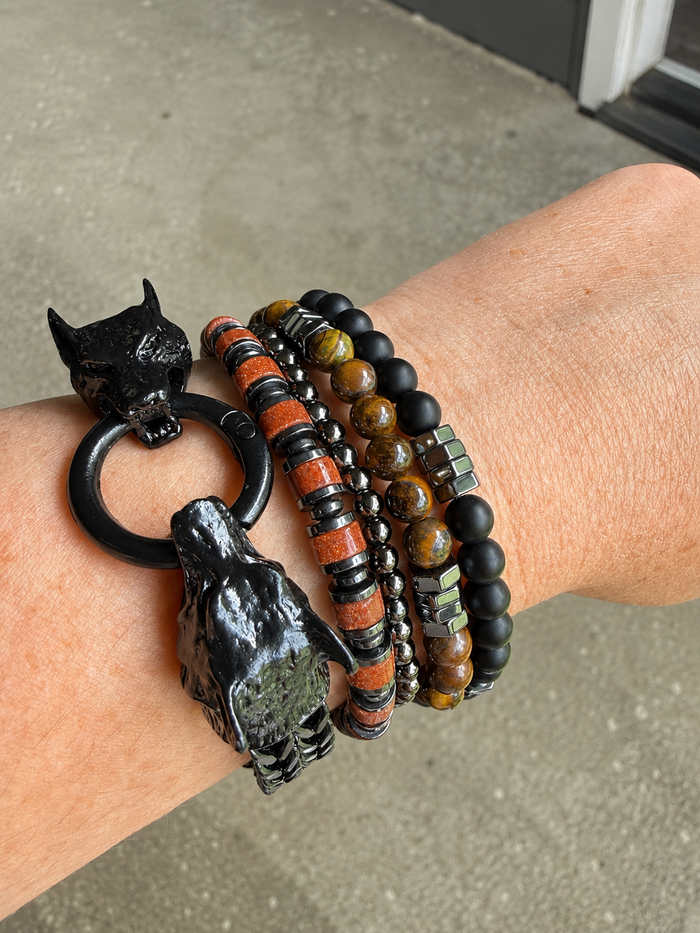 Wrist wearing Ulfur black cat-shaped bracelets with beaded design on a concrete surface.