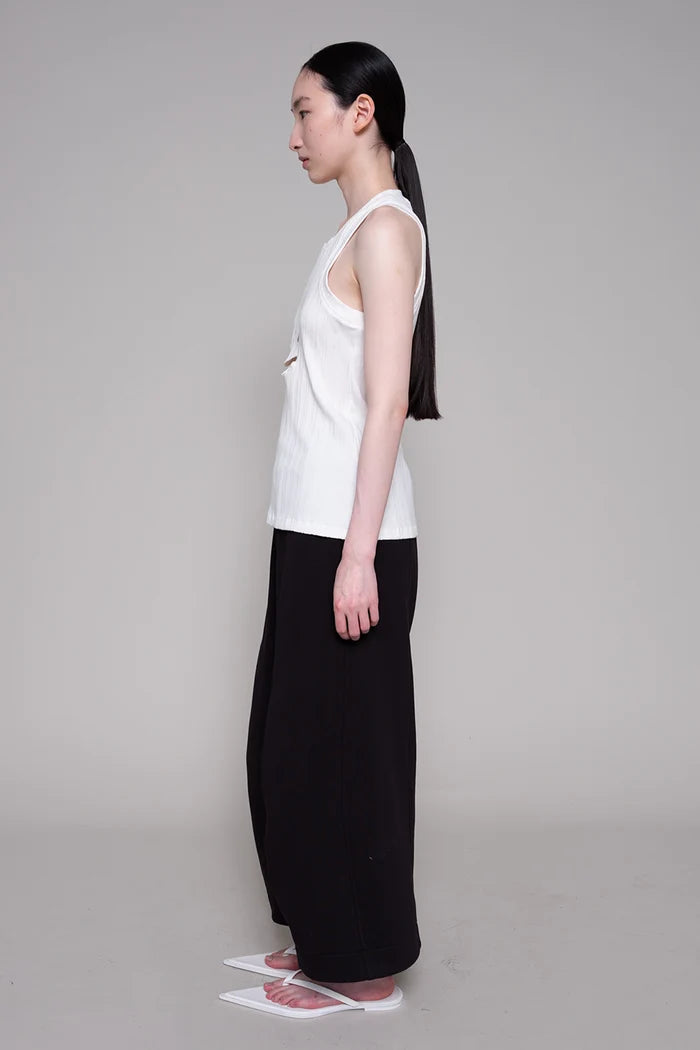 Woman wearing a white sleeveless top and black pants on a gray background