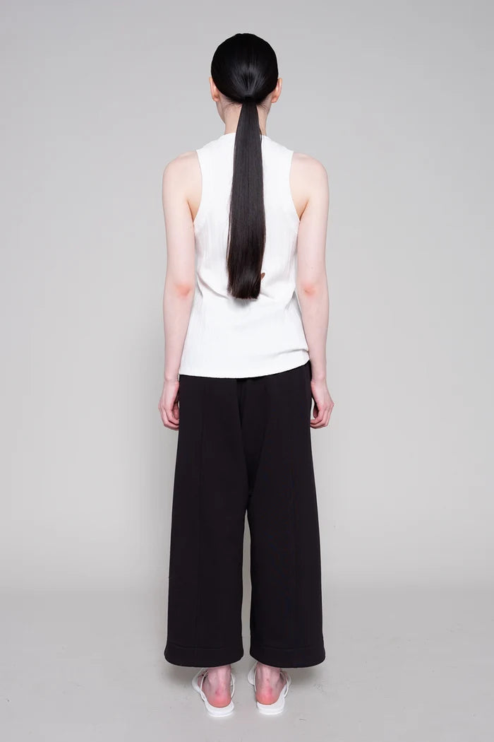 Person wearing a white sleeveless top and black wide-leg pants on a gray background